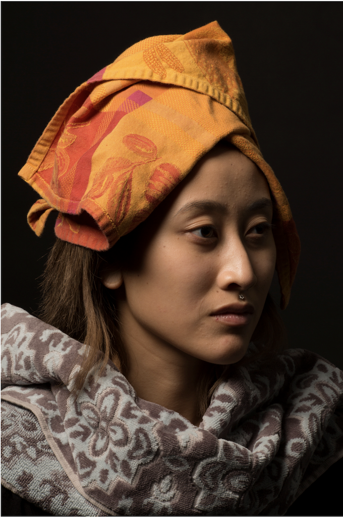 Color portrait of an Asian woman wearing a brown and light blue paisley top with an orange and red headscarf tied on her head.